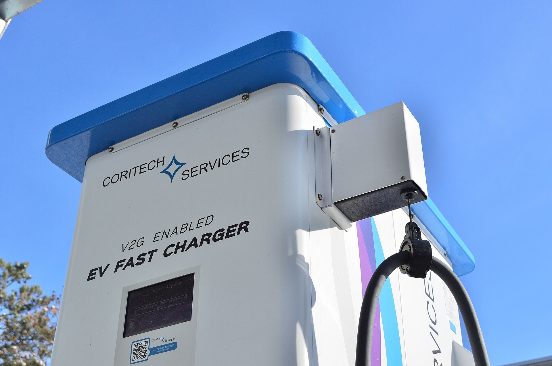 Low-angle view of a white and blue Coritech Services pedestal labeled V2G enabled EV fast charger, a DC unit with its inverter off the vehicle; the new UL 1741 supplement covers AC wallboxes for cars with onboard inverters