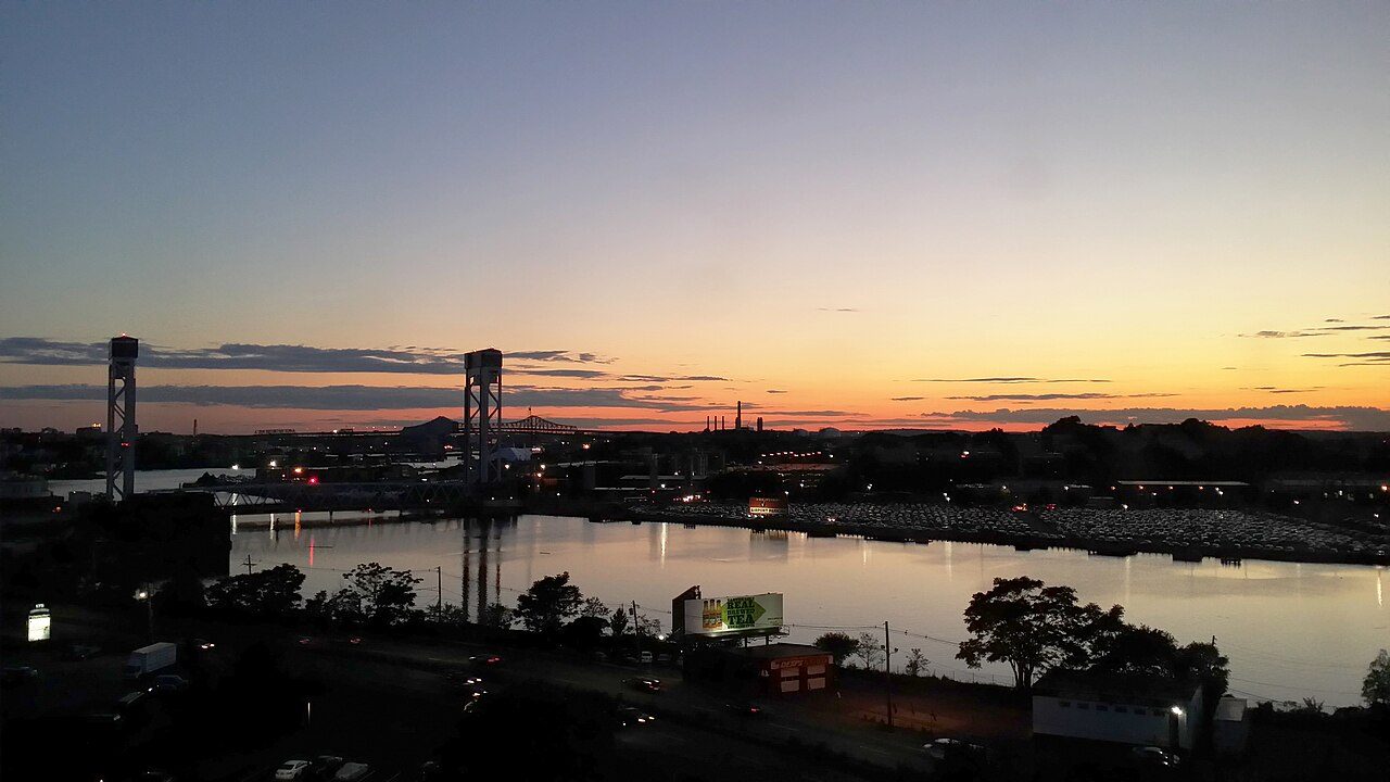 Dusk over Chelsea Creek, with the two lift towers of the Chelsea Street Bridge at left, rows of parked cars on the far bank and lit streets in the foreground.