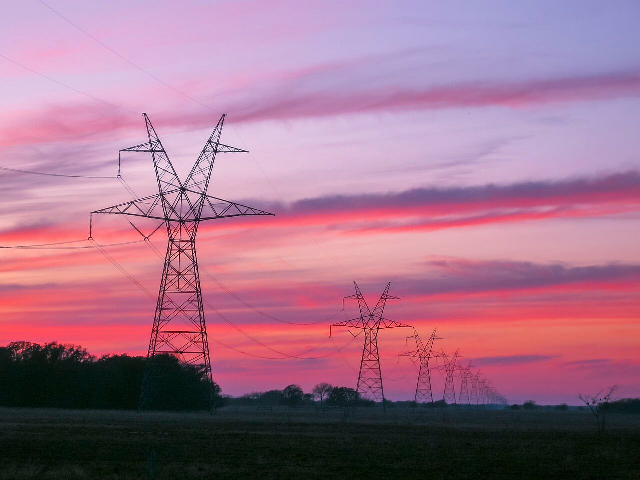 High-voltage transmission towers and lines silhouetted against a sunset
