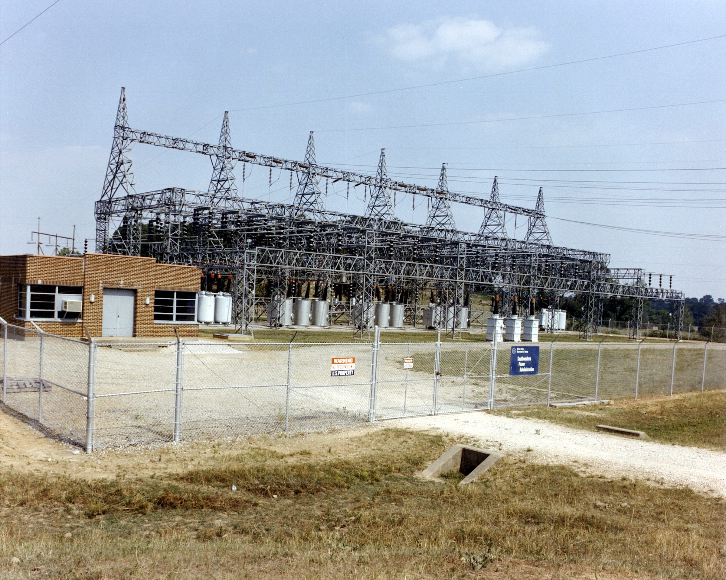 Rows of transformers and steel lattice towers in a fenced high-voltage substation switchyard