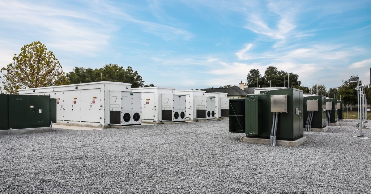 Rows of white battery enclosures and green transformer cabinets on a gravel pad at Duke Energy Florida's Trenton battery site