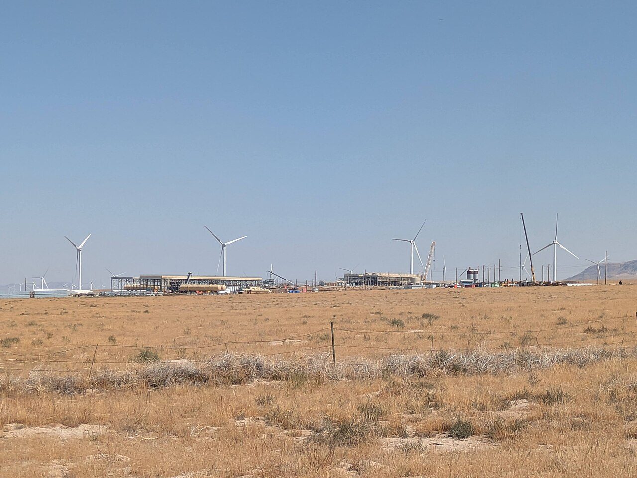 Cape Station Phase 1 geothermal power plant under construction near Milford, Utah, with wind turbines behind it, August 2025