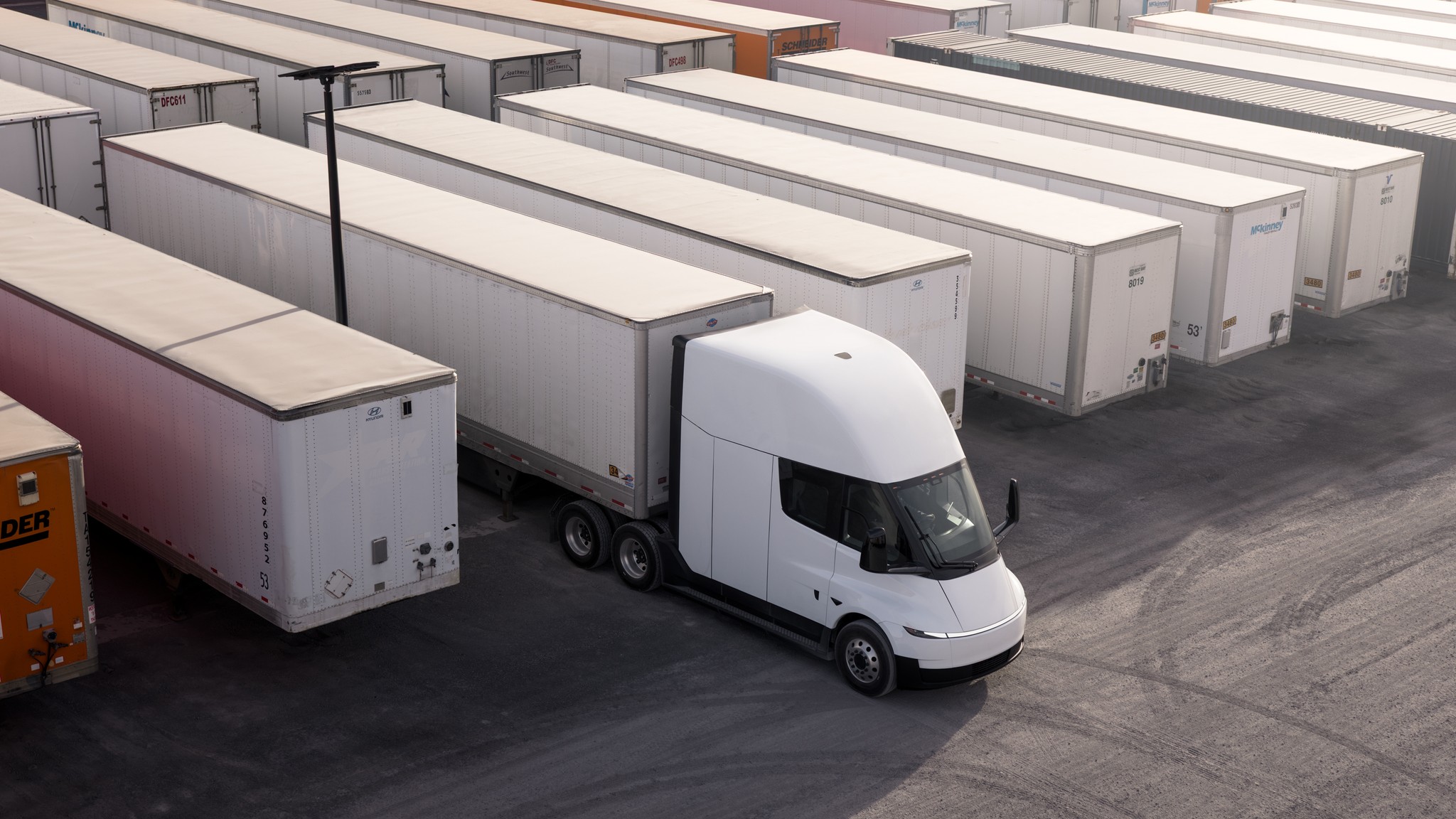 A white Tesla Semi tractor parked among rows of semi trailers in a freight yard