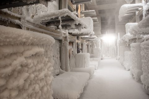Frost-coated heat pump units and overhead piping lining an aisle inside an indoor test chamber, with a bright light at the far end
