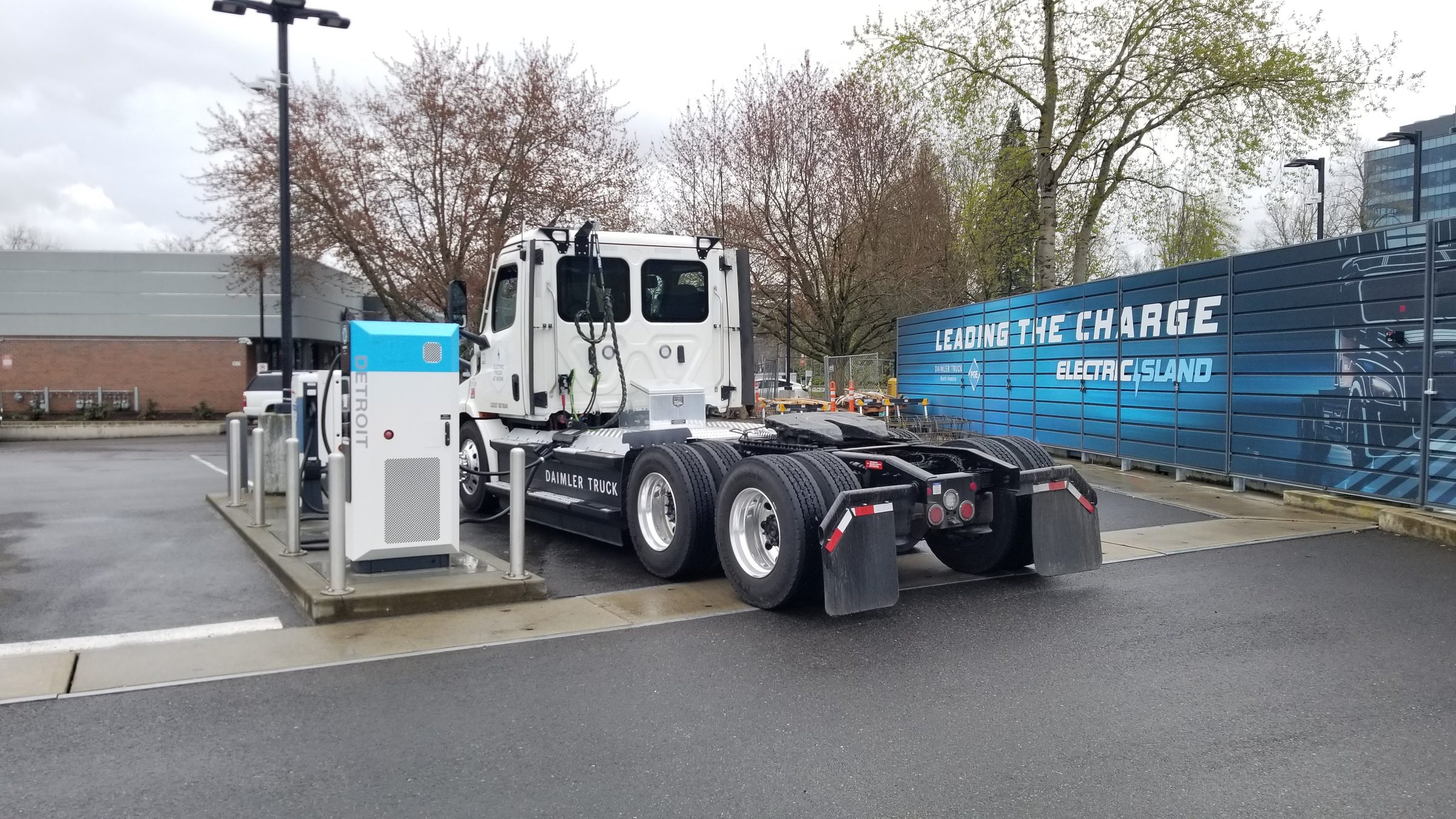 A white Freightliner eCascadia battery-electric Class 8 tractor plugged into a DC fast charger at a truck charging site