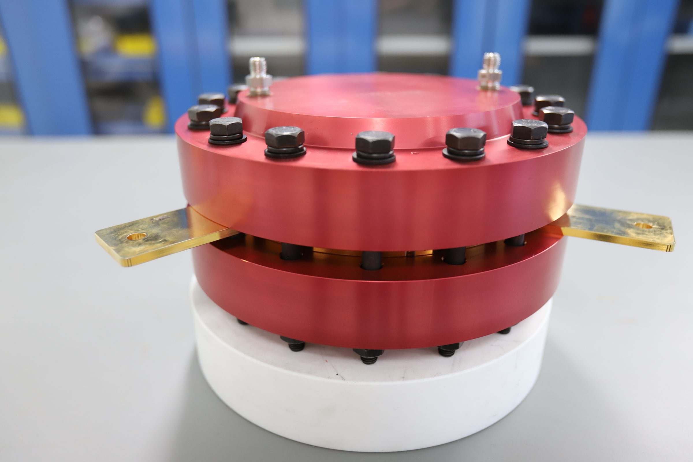 Electrochemical compressor stack: red anodized circular flanges bolted together with gold electrode tabs protruding from the sides