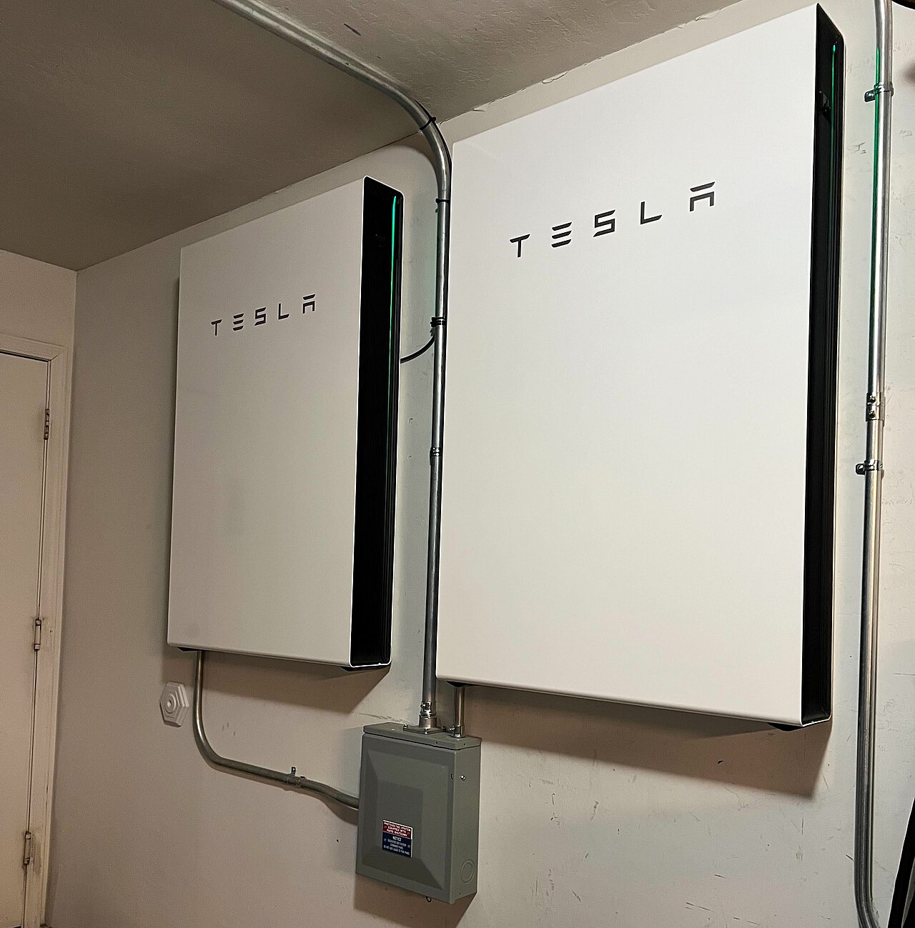 Two Tesla Powerwall 3 home batteries mounted on an interior wall beside a disconnect box