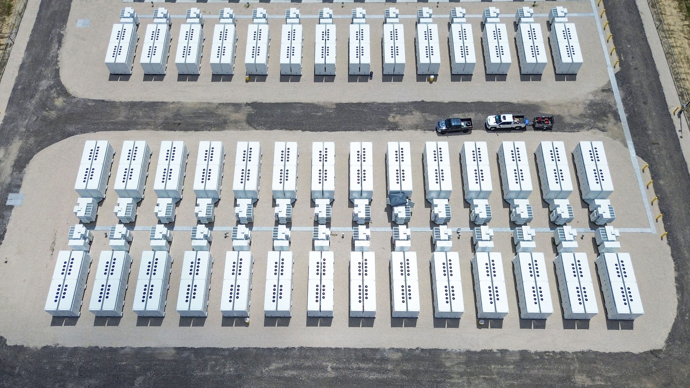 Aerial view of rows of white battery enclosures on gravel pads at Nightpeak Energy's Bocanova 2 site in Brazoria County, Texas, with two pickup trucks on an access road